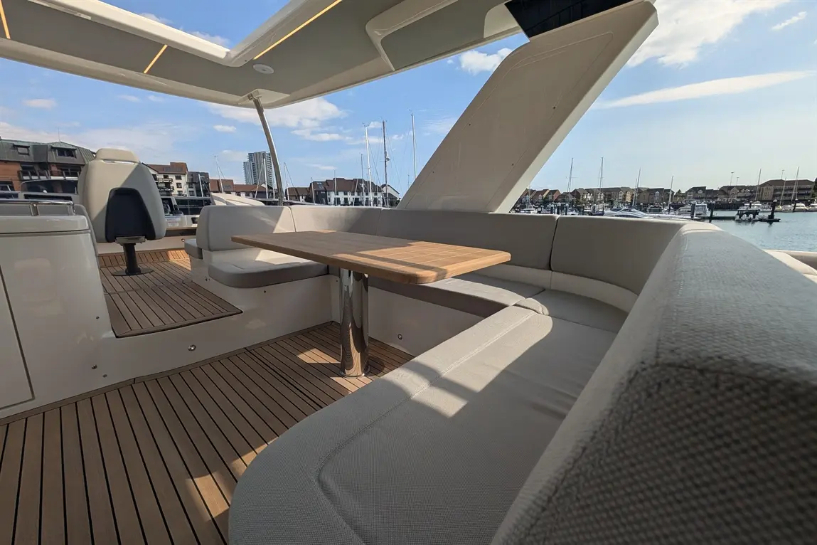 Luxury yacht interior featuring a wooden table, grey seating, and marina views under a blue sky. Ideal for relaxation.